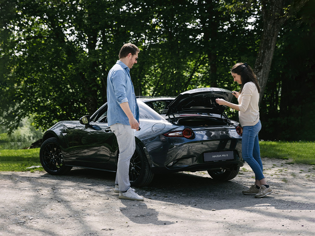 Der Mazda MX-5 mit offenem Kofferraum und zwei Personen vor dem Fahrzeug